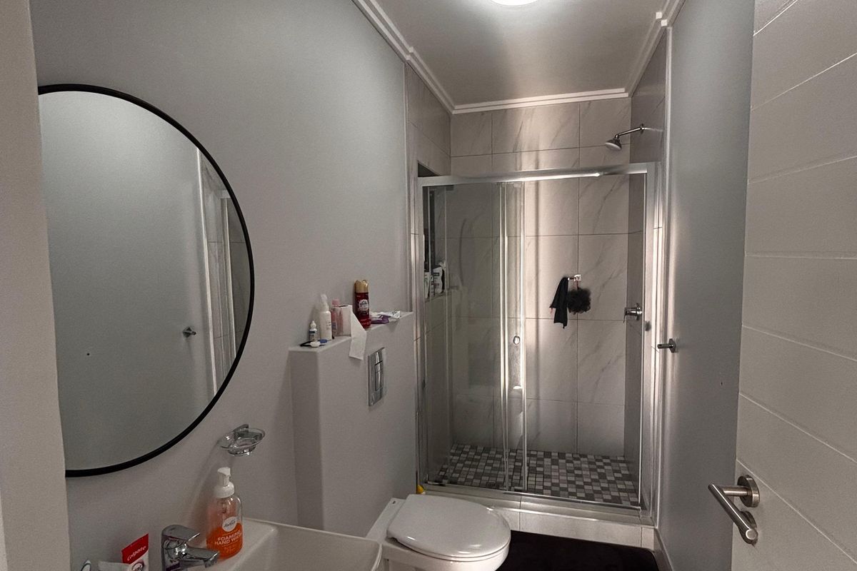 Modern bathroom featuring a wall-mounted toilet, a glass-enclosed shower with tiled flooring, and a sleek vanity basin with a circular mirror.