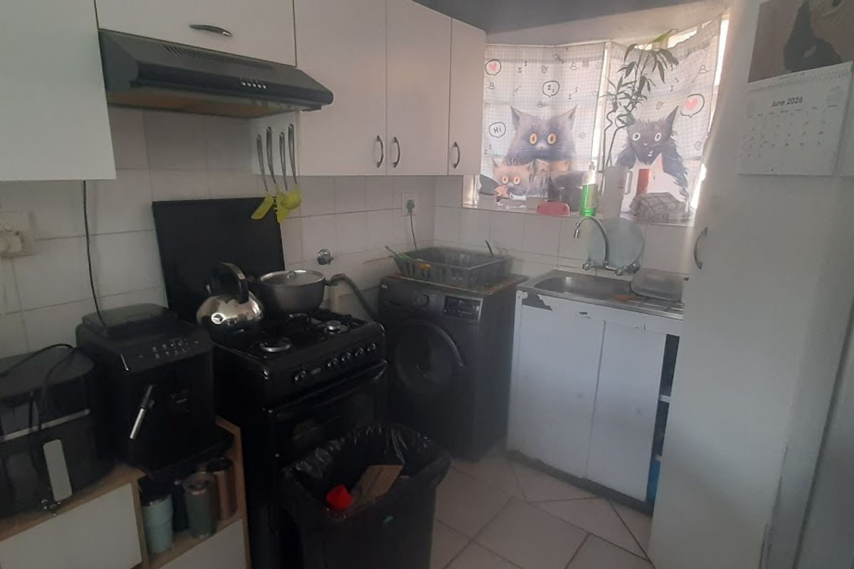 A compact kitchen featuring white cabinetry, a gas stove with extractor fan, and a built-in sink area with tiled splashbacks.