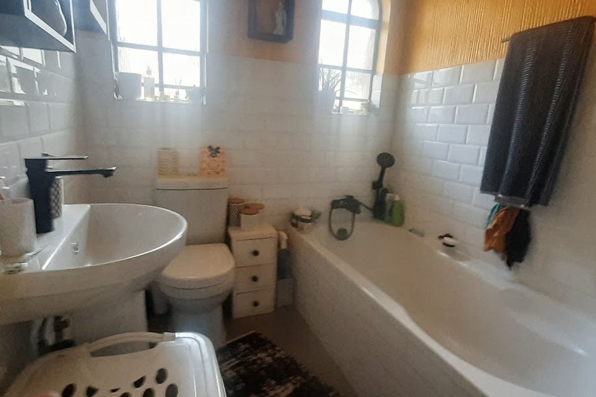 A compact bathroom featuring white subway wall tiles, a pedestal basin with modern black tapware, a standard bathtub, and two arched windows.