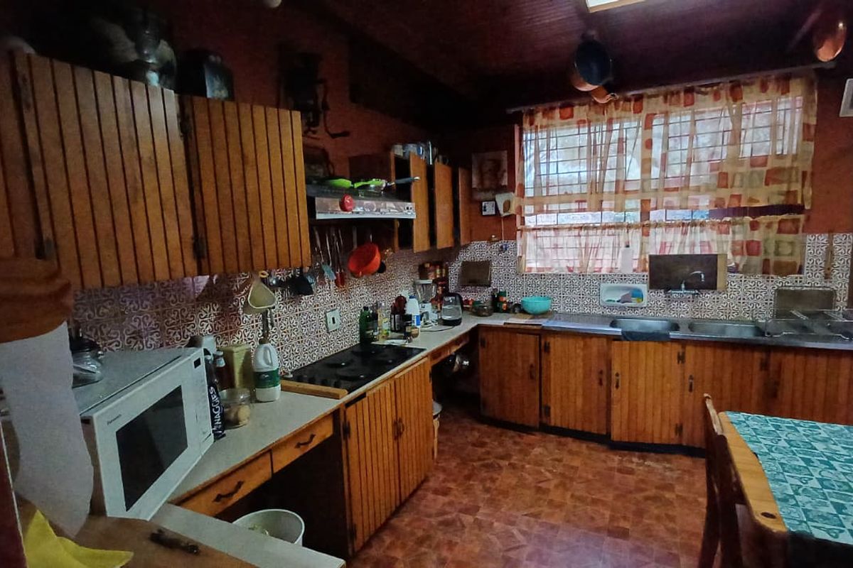 A rustic kitchen featuring wooden cabinetry, a patterned tile backsplash, integrated hob, and double sink, offering a traditional farm-style aesthetic.