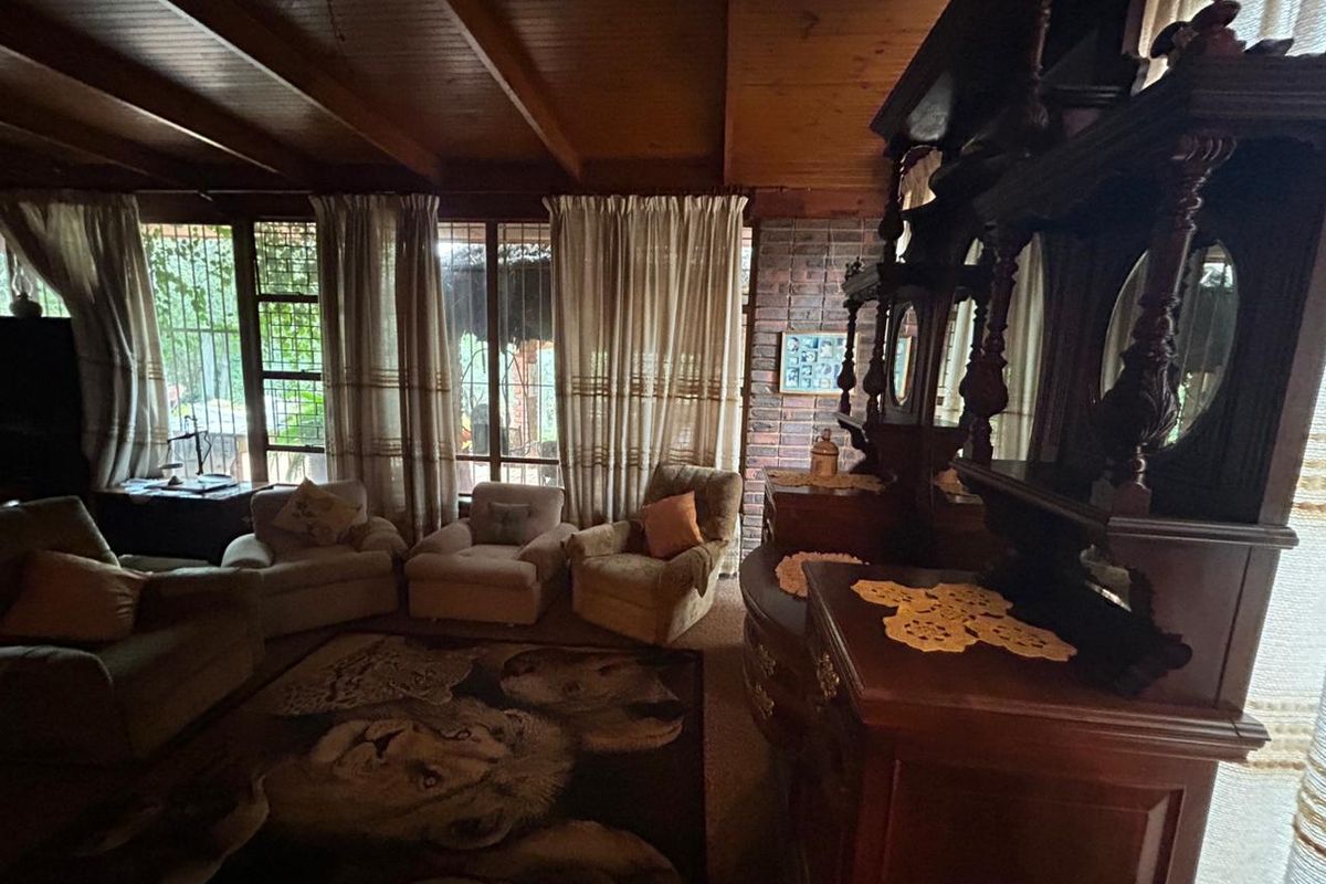 A cozy living room featuring exposed timber beam ceilings, a rustic brick feature wall, and large windows that provide ample natural light.