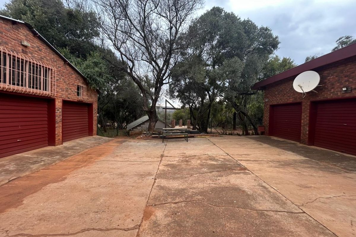 A spacious outdoor courtyard area situated between two brick garage structures, featuring a concrete driveway and mature trees in the background.