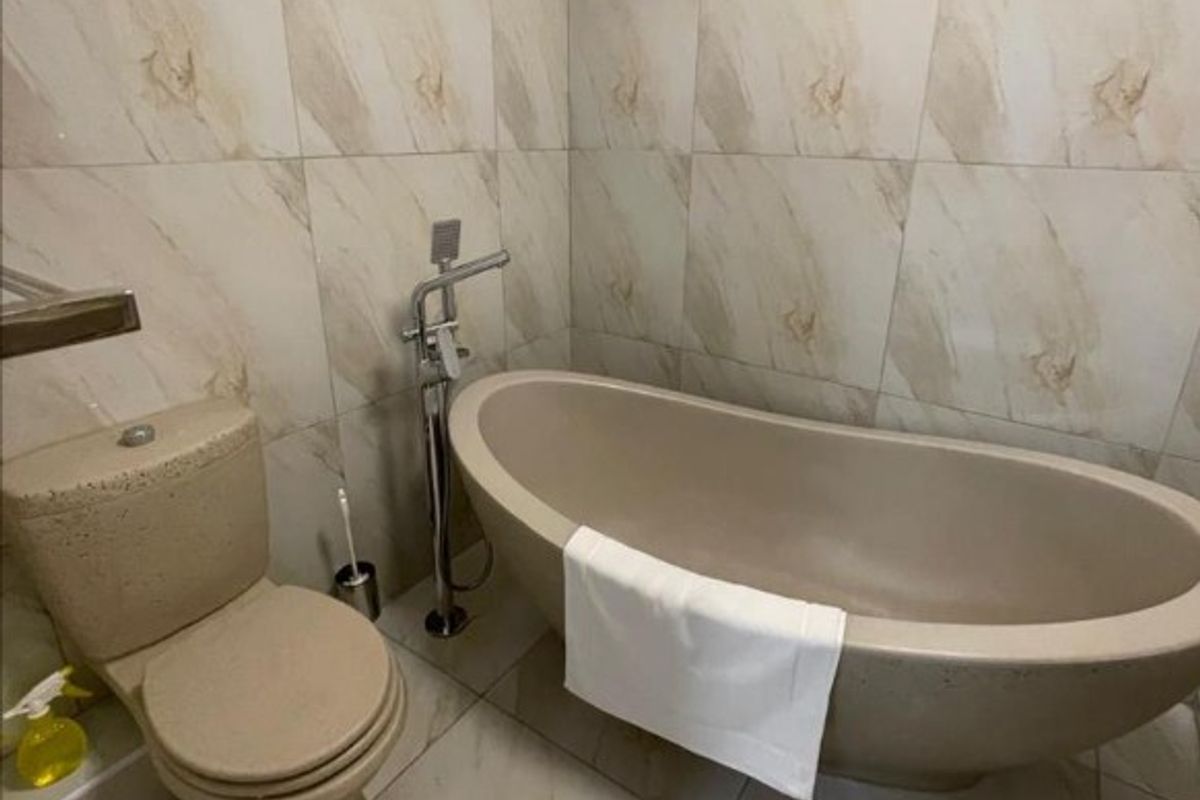 A modern bathroom featuring a freestanding bathtub, floor-mounted faucet, and a matching toilet, finished with neutral marble-effect wall and floor tiles.