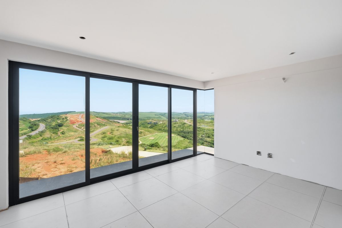 A bright, modern, and empty living space featuring large-format floor tiles and expansive floor-to-ceiling sliding glass doors with panoramic landscape views.