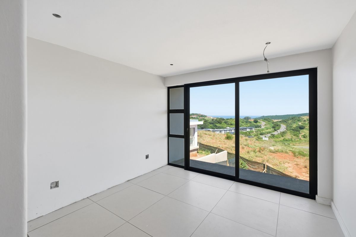 A bright, empty bedroom featuring large sliding glass doors that offer expansive views of the surrounding landscape and coastline.