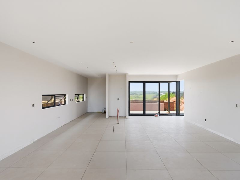 Spacious open-plan living area featuring large format floor tiles, recessed lighting, and expansive aluminium sliding doors leading to an outdoor view.