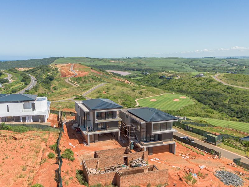Aerial view of modern residential properties under construction, featuring contemporary architectural design, metal roofing, and expansive views of the surrounding estate and golf course.