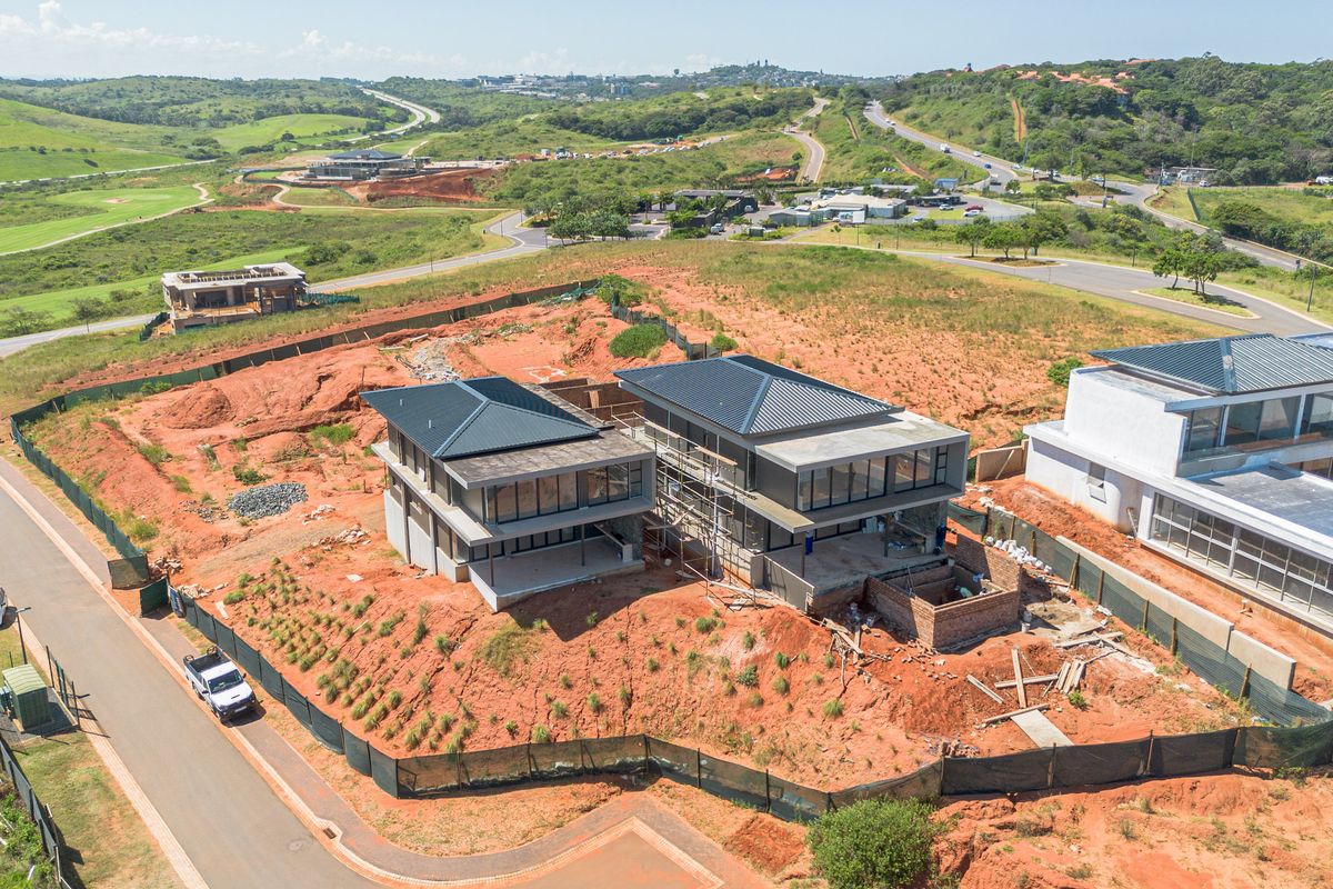 Aerial view of a residential property under construction, featuring modern architectural design with metal roofing and large glass facades in a developing estate.