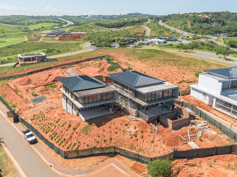 Aerial view of a residential property under construction, featuring modern architectural design with metal roofing and large glass facades in a developing estate.
