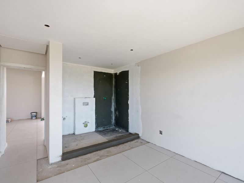 An unfinished bathroom space featuring a walk-in shower area, concealed cistern plumbing, and neutral floor tiling, currently undergoing renovation.