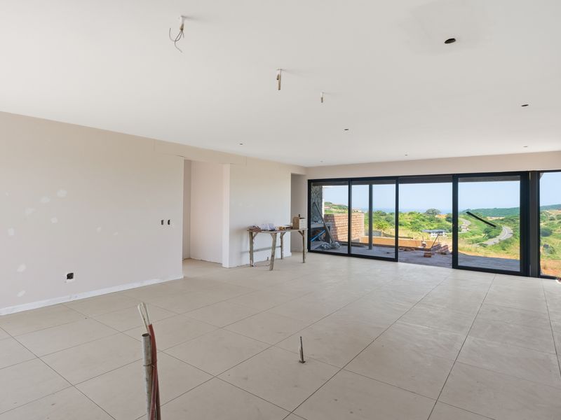 Spacious open-plan living area under construction, featuring large format floor tiles, sliding glass doors, and scenic views, awaiting final finishes and lighting installation.