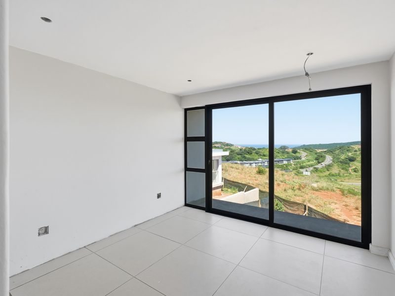 A bright, empty bedroom featuring large sliding glass doors that offer expansive views of the surrounding landscape and coastline.