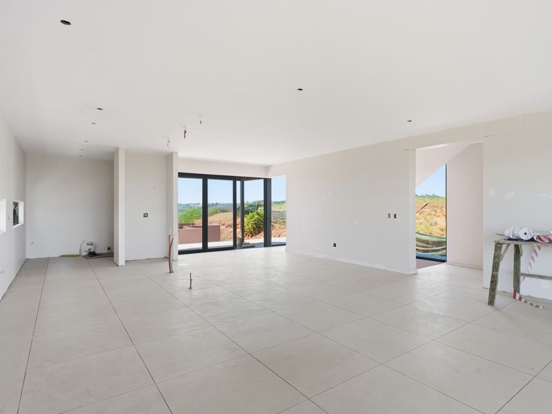 Spacious open-plan living area under construction, featuring large format floor tiles, modern black aluminium sliding doors, and neutral plastered walls ready for finishing.