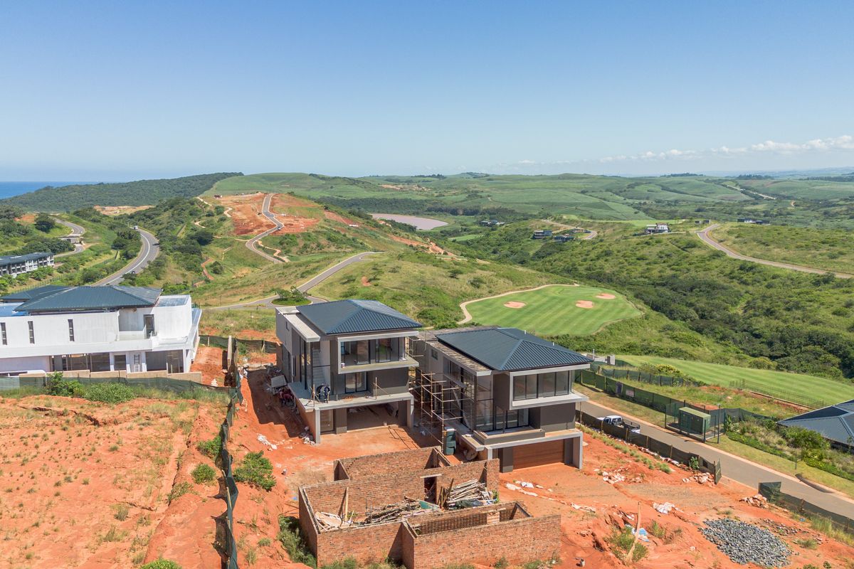 Aerial view of modern residential properties under construction, featuring contemporary architectural design, metal roofing, and expansive views of the surrounding estate and golf course.