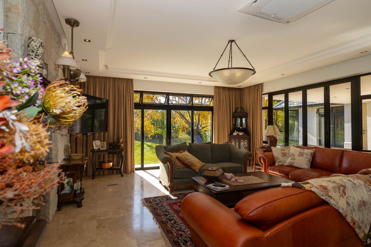 Spacious living room featuring stone flooring, a stone fireplace, and large black-framed glass doors providing seamless access to the garden.