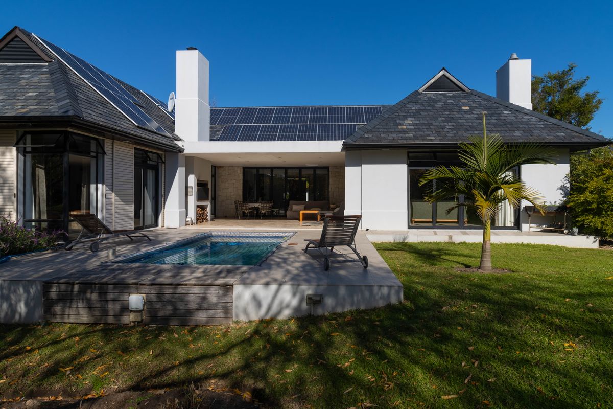 Rear exterior view featuring a swimming pool, covered patio with built-in fireplace, solar panels, and well-maintained garden area.