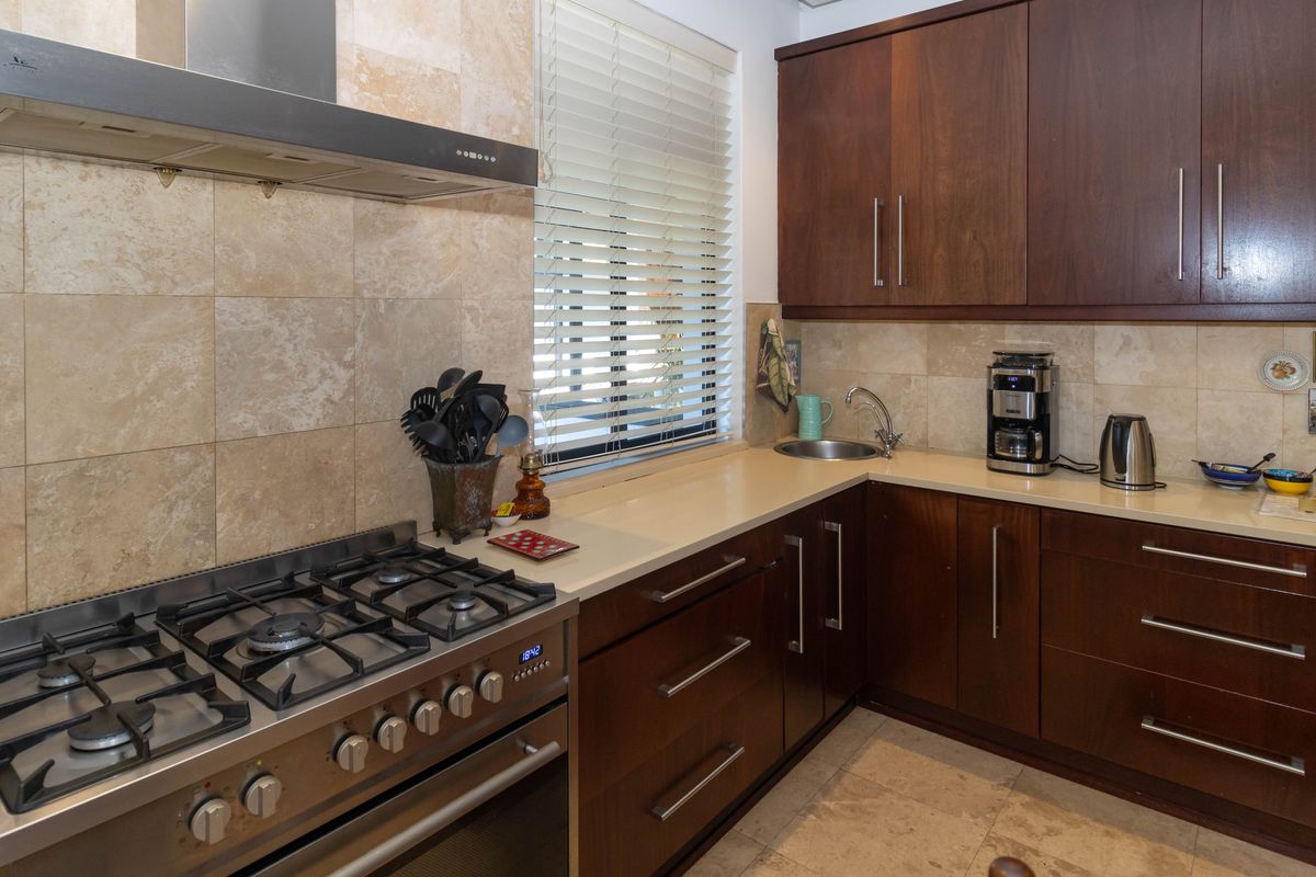 A functional kitchen featuring dark wood cabinetry, stone countertops, a gas stove with an extractor fan, and a tiled backsplash.