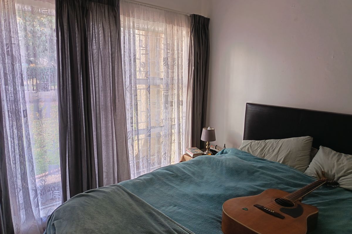 A bedroom featuring large windows with curtains, providing natural light and a view of the garden area.