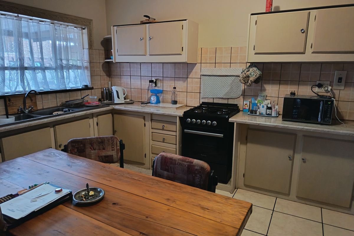 A dated kitchen featuring original cabinetry, tiled splashbacks, and a freestanding gas stove, offering potential for a modern renovation.