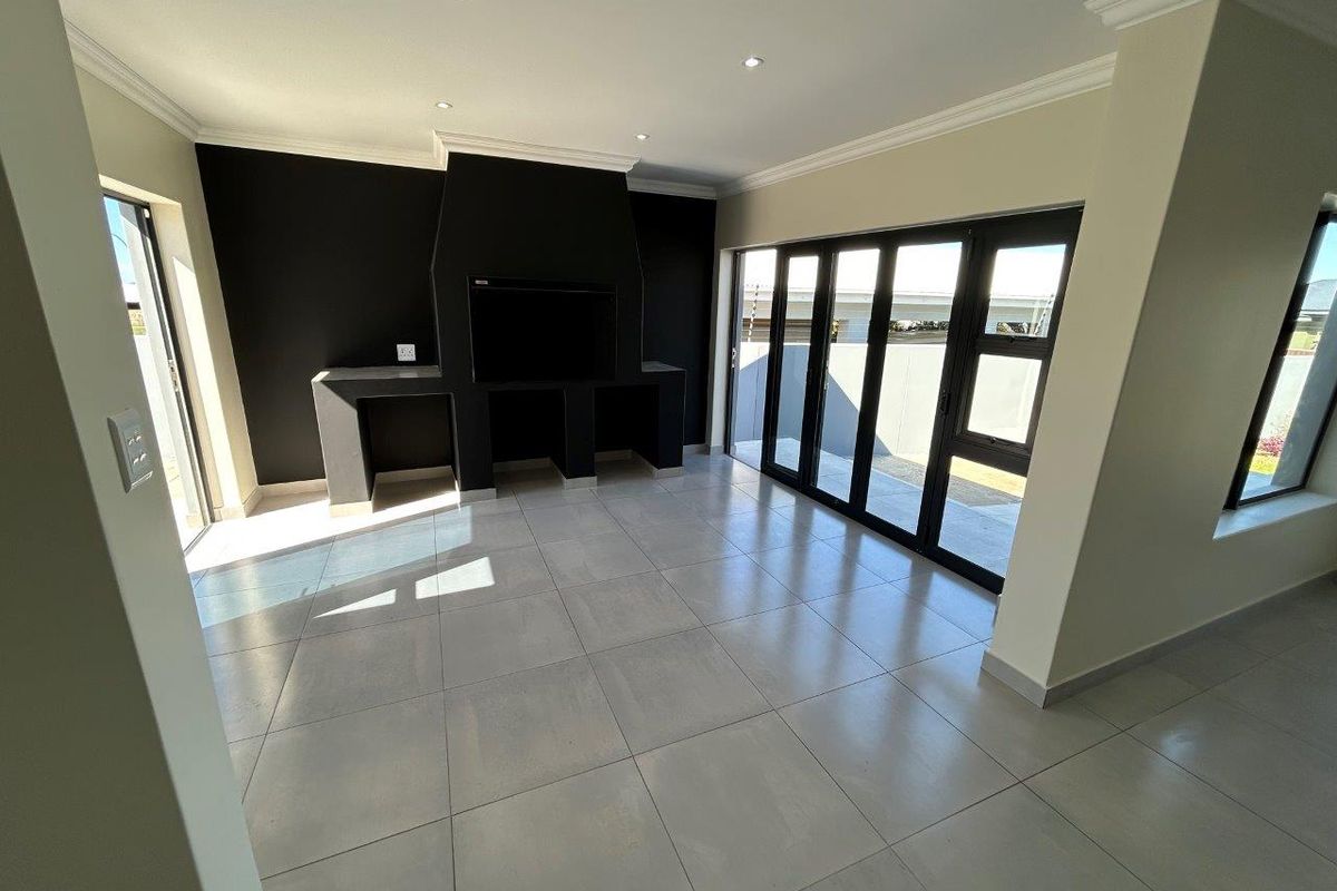Spacious living area featuring large format floor tiles, a built-in fireplace, and expansive black-framed stacker doors leading to the outdoor space.