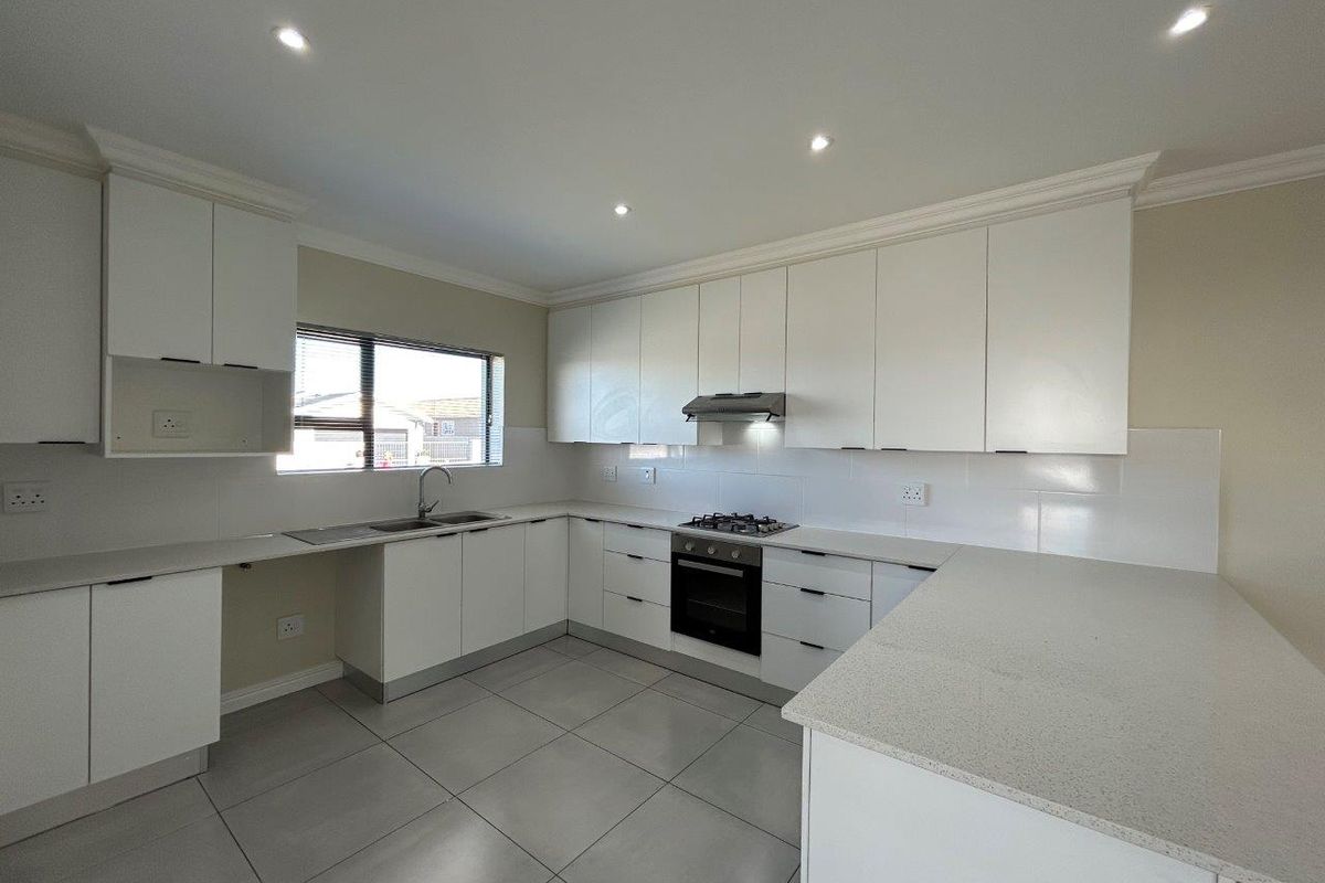 Modern kitchen featuring white cabinetry, stone countertops, tiled flooring, built-in oven, gas hob, and stainless steel extractor fan.