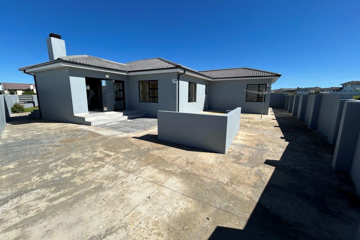 Rear view of the house featuring a paved courtyard, concrete boundary walls, and a chimney stack.