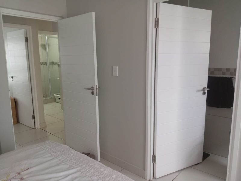 A view of a hallway leading to a bathroom, featuring modern white horizontal-panel doors and tiled flooring throughout.