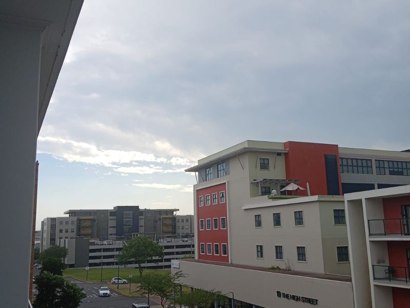 An elevated street view from a balcony overlooking a modern urban neighborhood with surrounding apartment buildings and street-level parking.