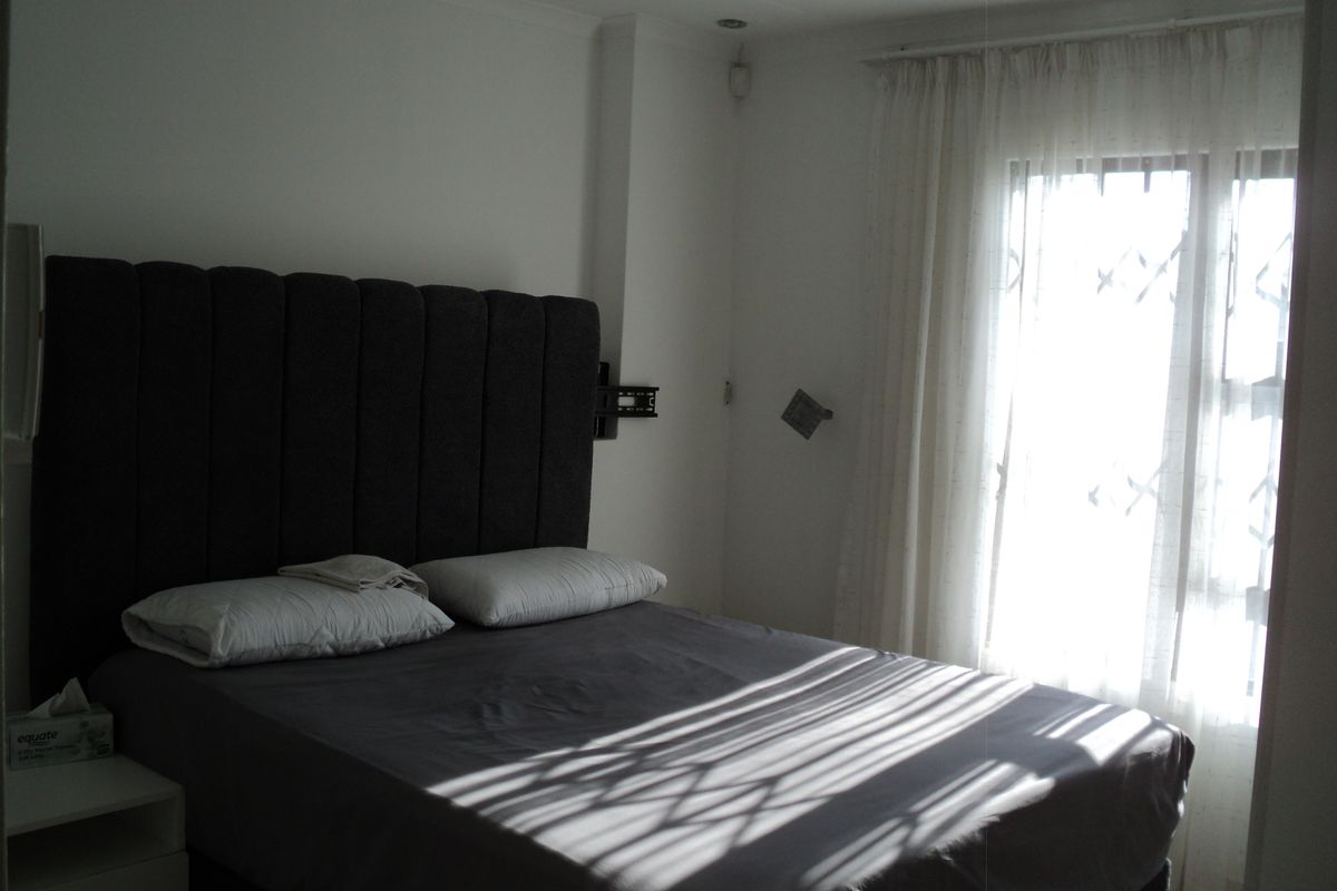 A bedroom featuring a window with a security gate and curtain tracks, illuminated by natural light.