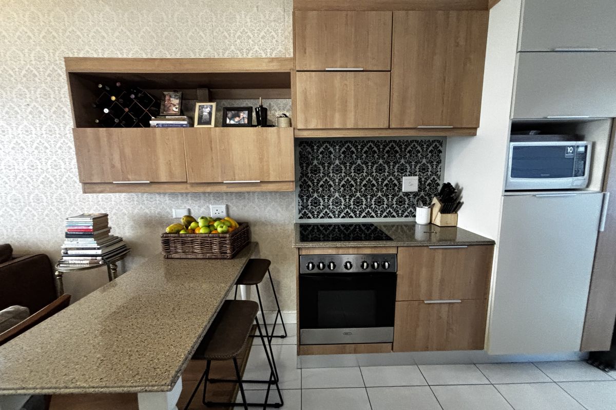 Compact kitchen featuring wood-finish cabinetry, granite countertops, a built-in oven with hob, and a decorative tiled backsplash, integrated with a breakfast bar area.