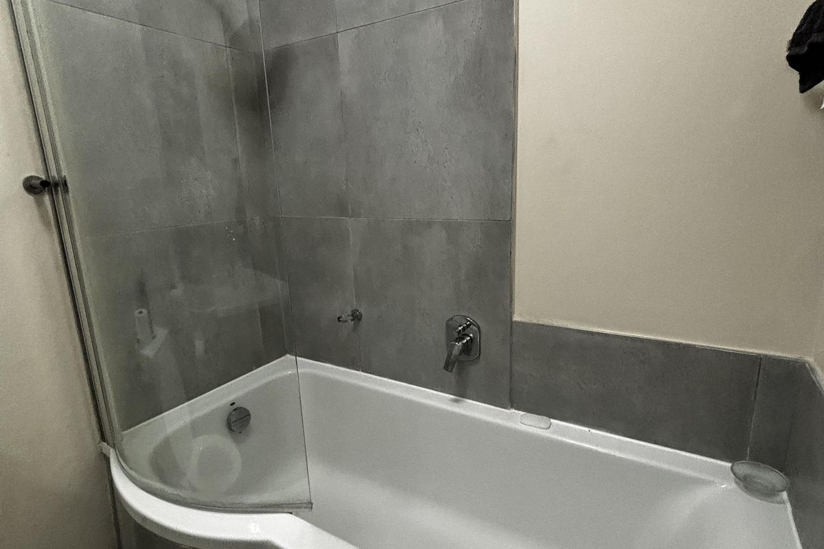 Modern bathroom featuring a P-shaped shower-bath combination with a glass screen and grey tiled surround.