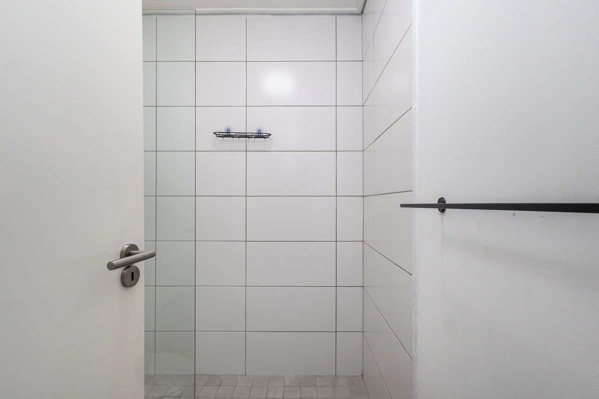 A clean, modern bathroom shower area featuring white wall tiles, a glass shower screen, and a black towel rail.