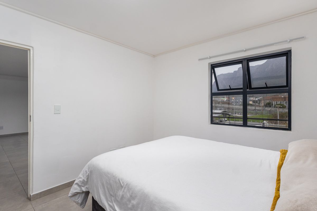 A bright bedroom featuring neutral walls, tiled flooring, and a modern black-framed window offering scenic mountain views.
