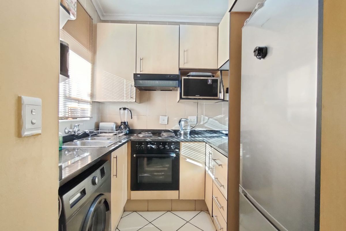 Compact kitchen featuring light-toned cabinetry, dark granite countertops, built-in oven, extractor fan, and integrated space for a washing machine.