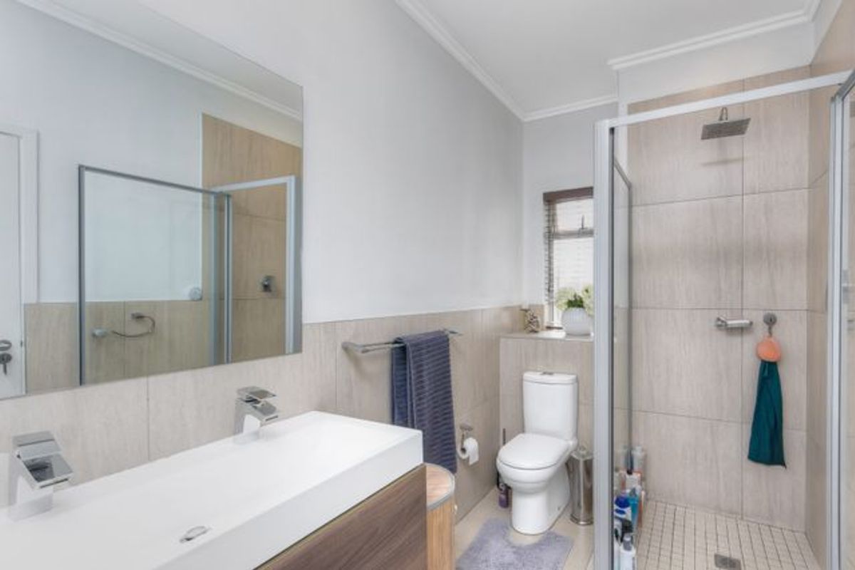 Modern bathroom featuring a floating vanity with basin, large wall mirror, and a glass-enclosed walk-in shower with neutral wall tiling.