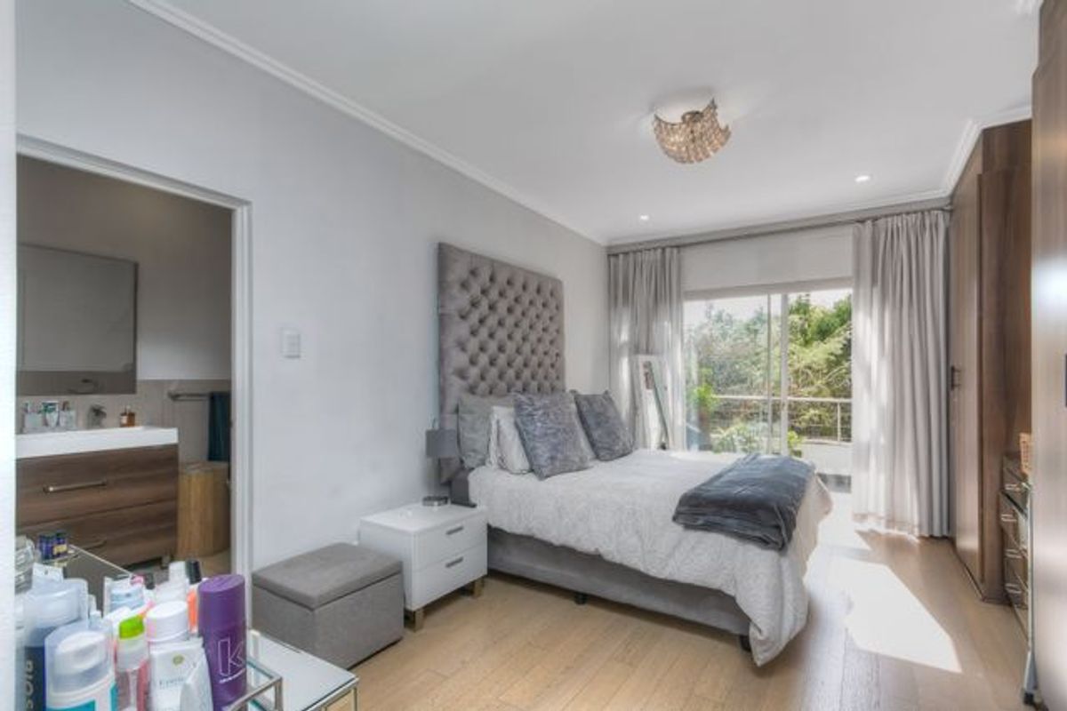 A bright bedroom featuring light wood flooring, built-in wardrobes, and an en-suite bathroom, with direct access to a private balcony.