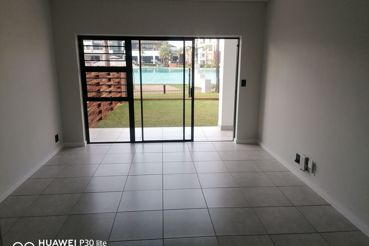 A bright, empty living area featuring large sliding glass doors that open onto a private patio with views of the communal pool area.