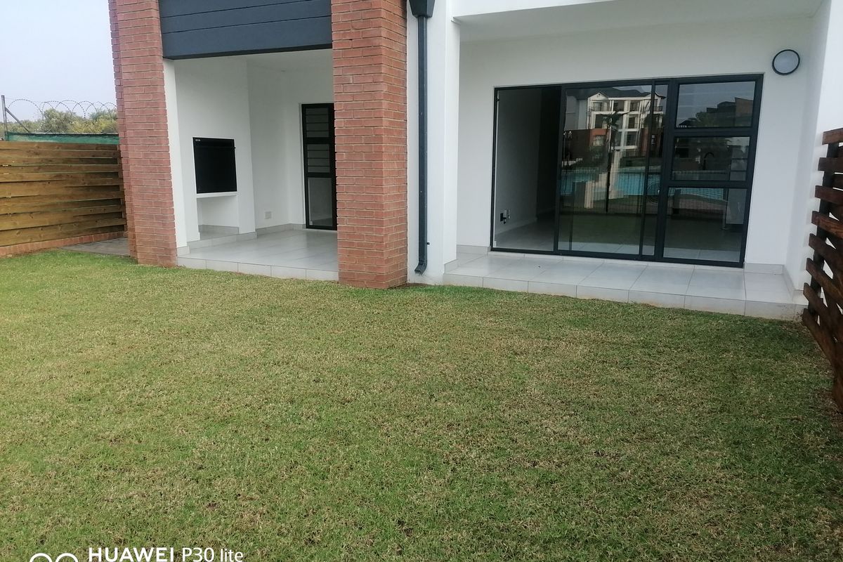 A private rear garden featuring a covered patio with a built-in braai and sliding glass doors leading into the apartment interior.