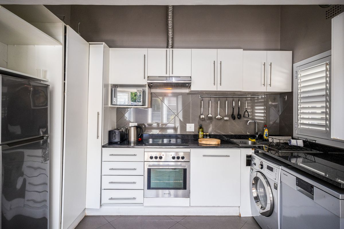 A compact, functional kitchen featuring white cabinetry, dark granite countertops, a built-in oven, hob, extractor fan, and integrated laundry plumbing.