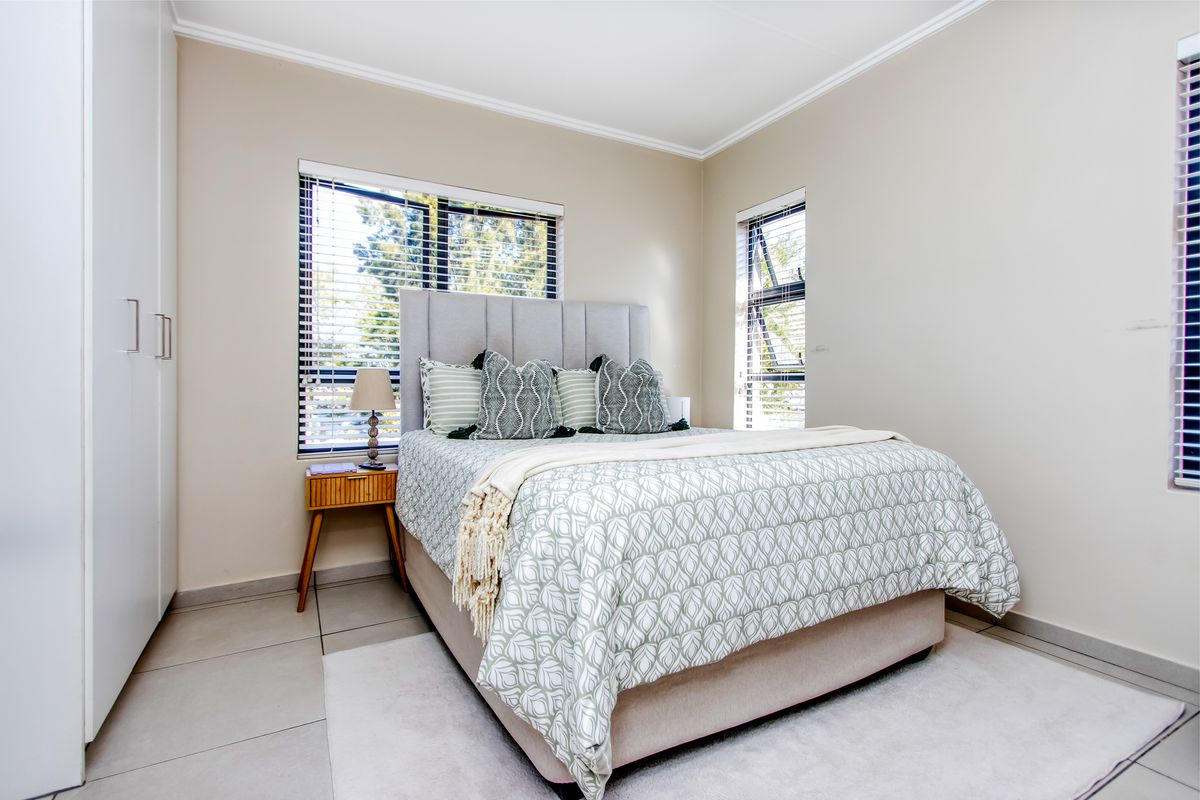 A well-maintained bedroom featuring neutral wall tones, tiled flooring, built-in cupboards, and large windows with fitted blinds.