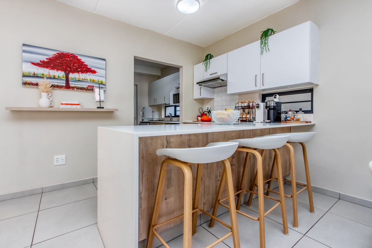 Modern kitchen featuring a breakfast bar with wood-look cabinetry, white upper cabinets, subway tile backsplash, and an integrated extractor fan.