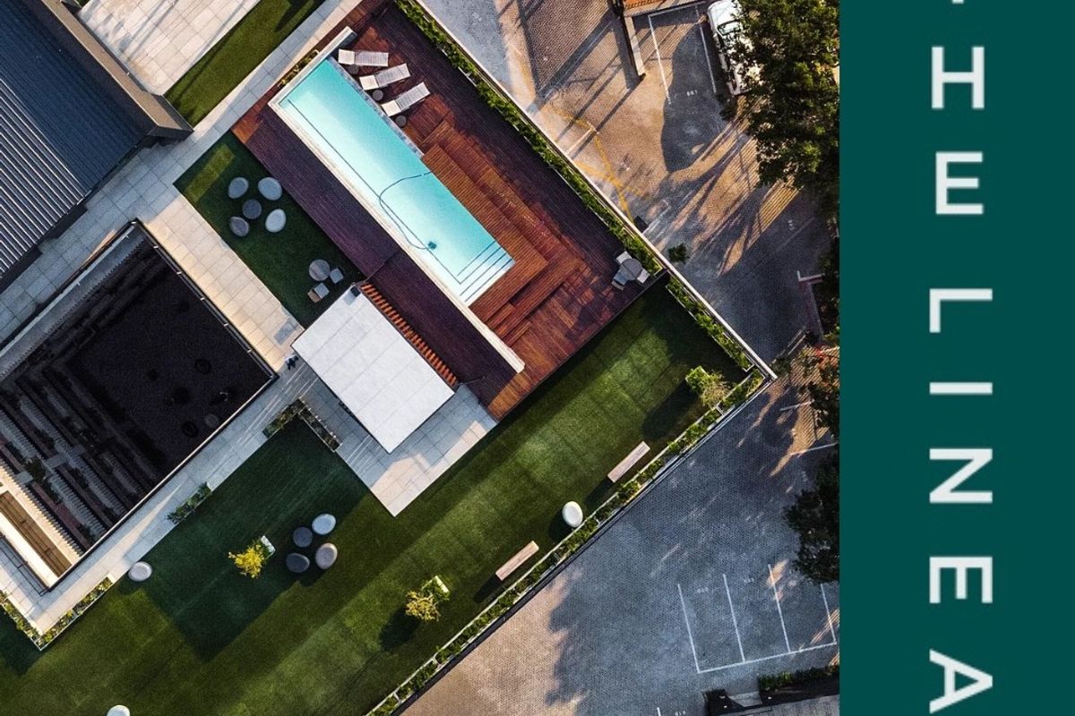 Aerial view of the apartment complex featuring a swimming pool with timber decking, landscaped green spaces, and designated parking areas.