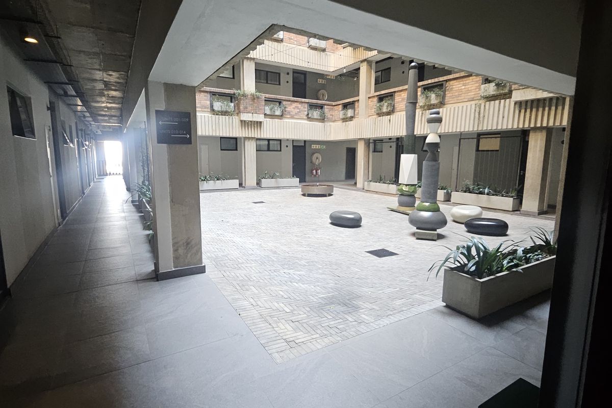 A view of an open-air central courtyard within an apartment complex, featuring paved flooring, concrete structural elements, and built-in planters.