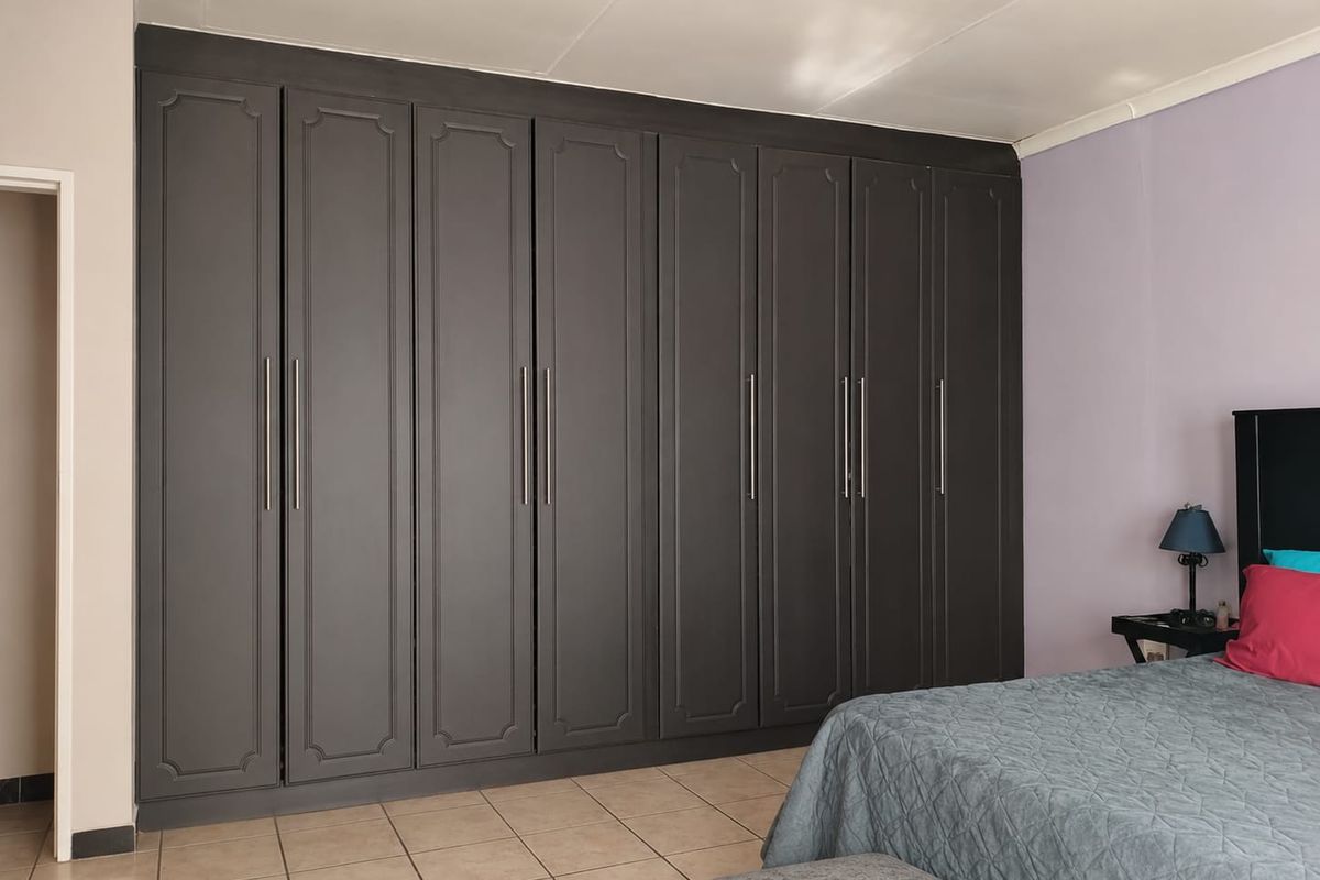 A bedroom featuring extensive floor-to-ceiling built-in cabinetry with dark grey panelled doors and modern metal handles.