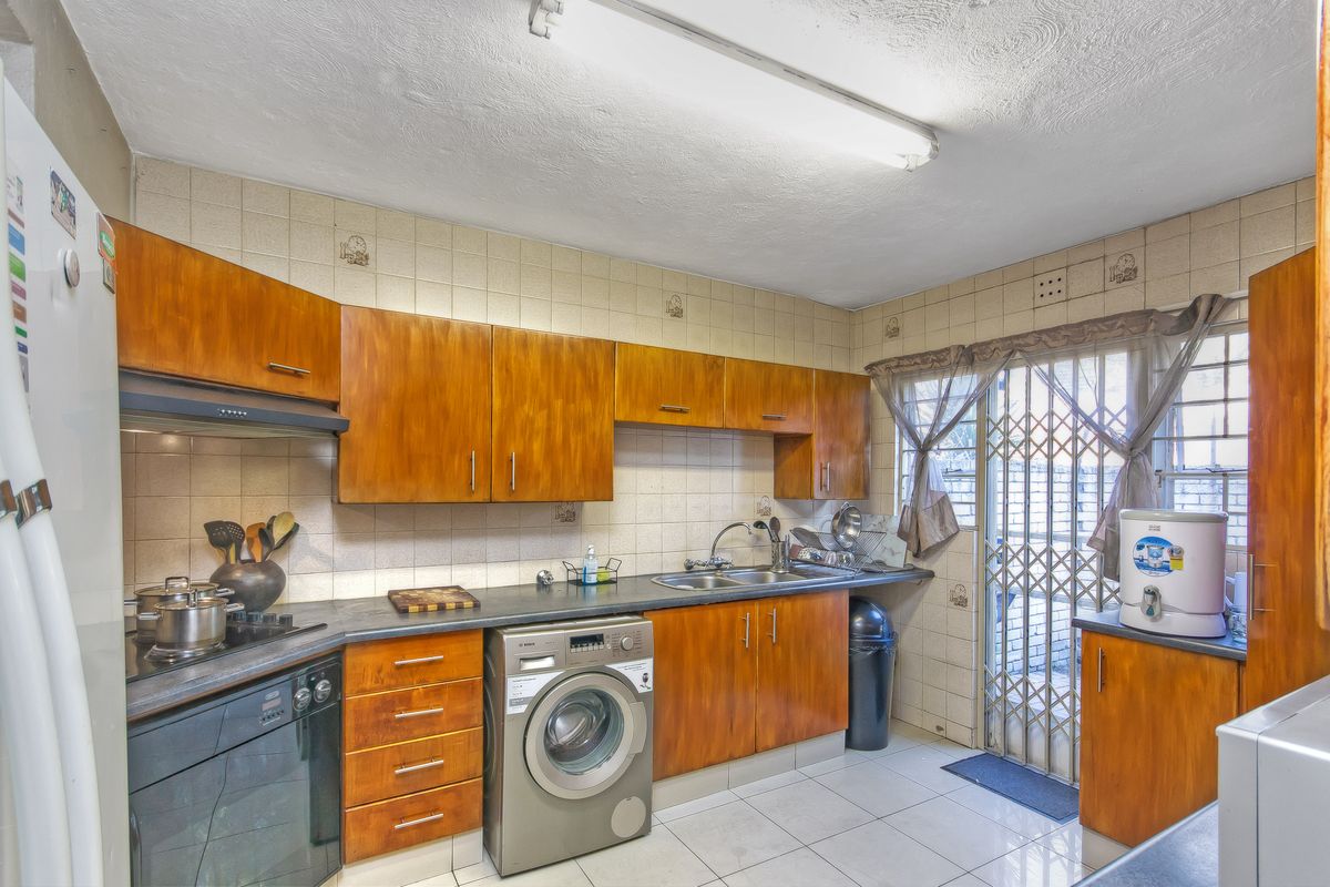 Functional kitchen featuring wood-veneer cabinetry, tiled splashbacks, integrated oven and hob, and a dedicated laundry connection point with direct access to the exterior.