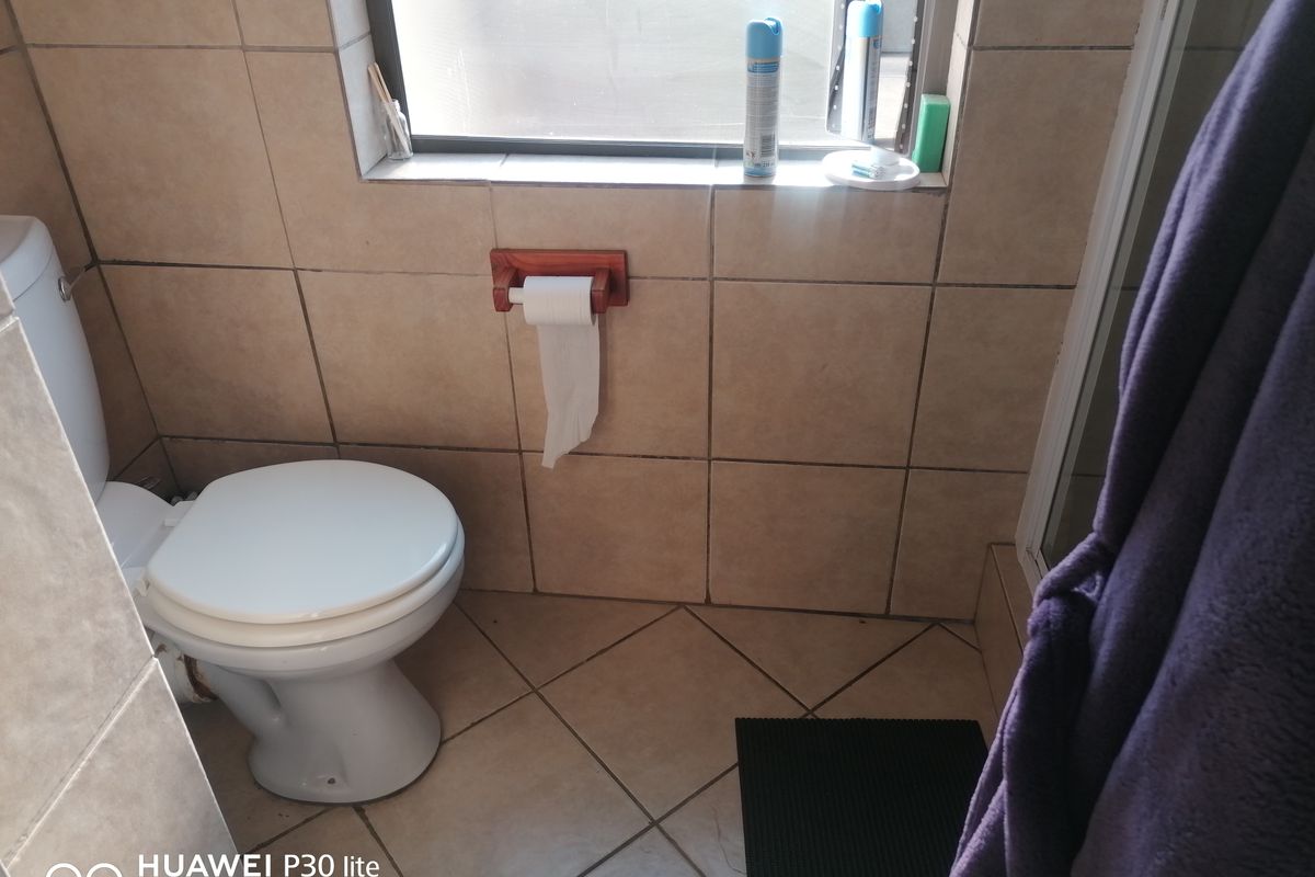 A functional bathroom featuring ceramic wall and floor tiling, a standard toilet, and a window providing natural light.