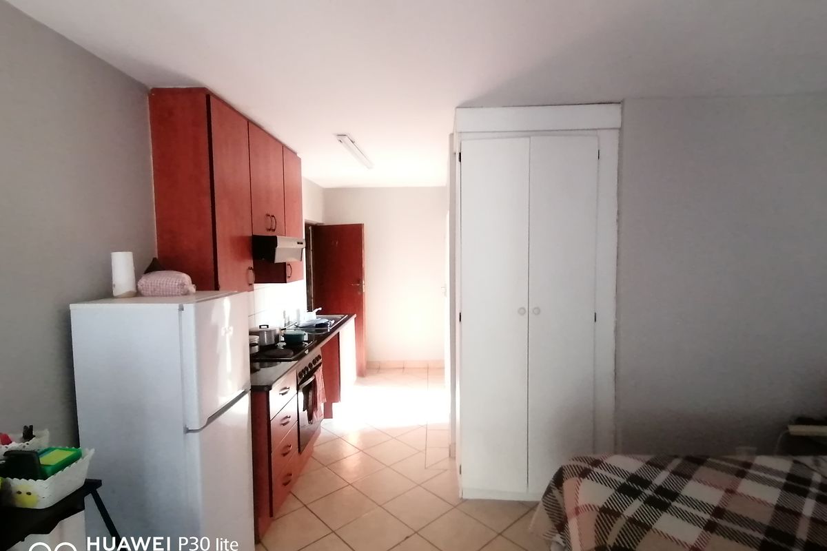 Compact kitchen area featuring dark wood cabinetry, integrated stove and extractor fan, tiled flooring, and a built-in storage cupboard.
