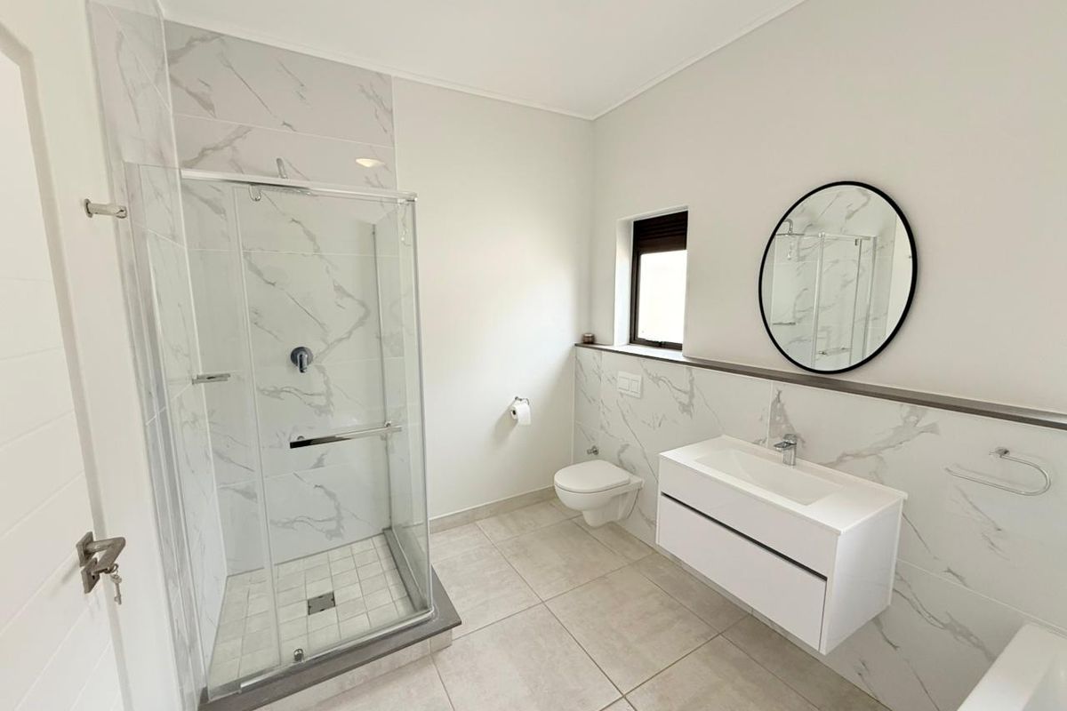 Modern bathroom featuring a glass-enclosed shower, wall-mounted vanity with basin, and a wall-hung toilet, finished with marble-look wall tiles and neutral floor tiling.