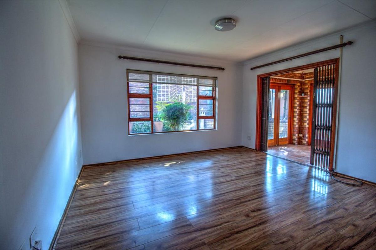 Spacious living area featuring wood-look laminate flooring, large window with security bars, and sliding door access to an enclosed patio area.