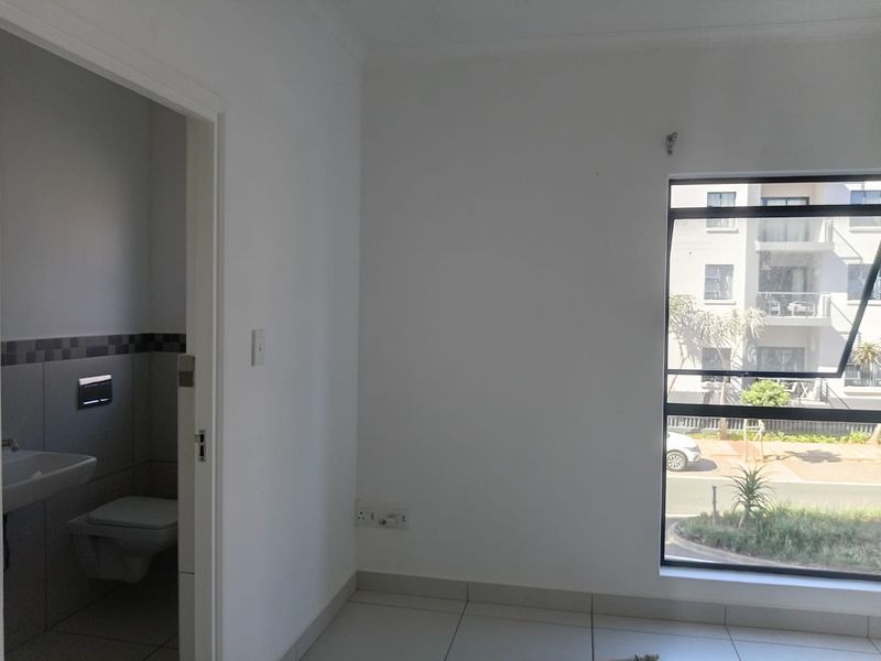 A bright, empty bedroom featuring tiled flooring, a large window, and an adjoining en-suite bathroom with modern fixtures.